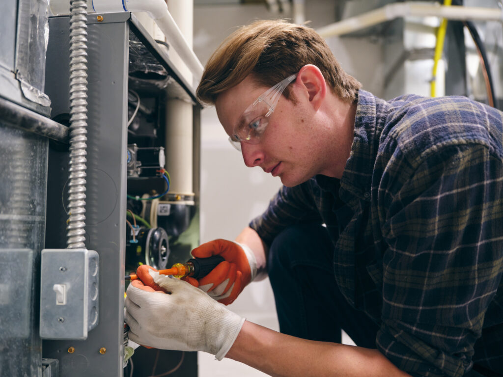 A furnace repairman working inside a home, repairing a furnace.